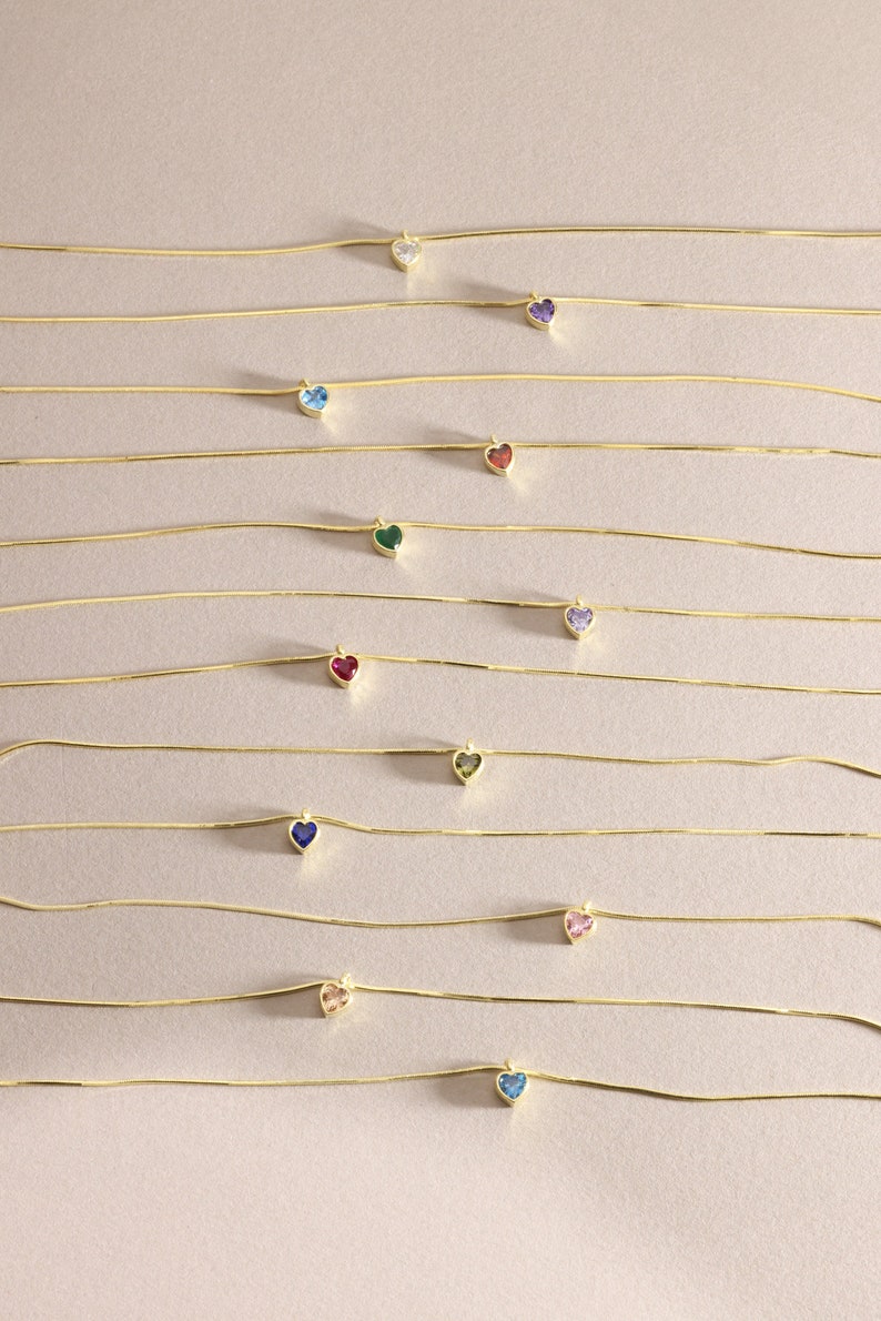 Puede incluir: Un conjunto de 12 collares de cadena de oro con colgantes en forma de coraz&oacute;n. Cada colgante presenta una gema de color diferente, incluyendo transparente, morado, azul, rojo, verde, y m&aacute;s.