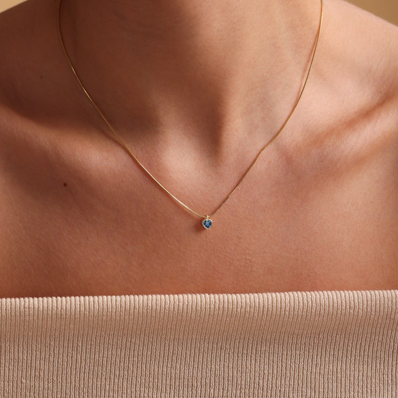 Puede incluir: Un collar de cadena de oro con un peque&ntilde;o colgante de coraz&oacute;n azul.