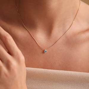 Puede incluir: Un delicado collar de cadena de oro con un peque&ntilde;o colgante de coraz&oacute;n azul.