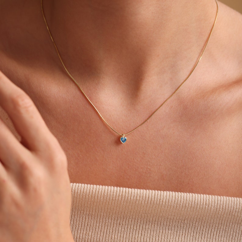 Puede incluir: Un delicado collar de cadena de oro con un peque&ntilde;o colgante de coraz&oacute;n azul.