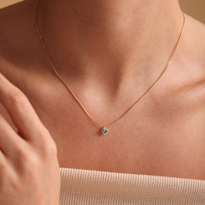 Puede incluir: Un delicado collar de cadena de oro con un peque&ntilde;o colgante de coraz&oacute;n azul.
