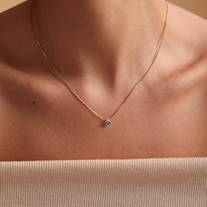 Puede incluir: Un delicado collar de cadena de oro con un peque&ntilde;o colgante de coraz&oacute;n azul.