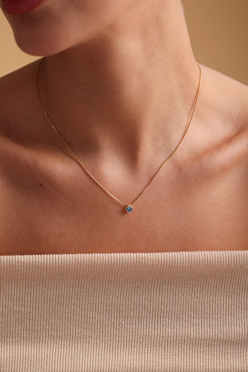 Puede incluir: Un delicado collar de cadena de oro con un peque&ntilde;o colgante de coraz&oacute;n azul.