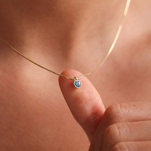 Puede incluir: Un delicado collar de cadena de oro con un peque&ntilde;o colgante de coraz&oacute;n con una piedra preciosa azul.
