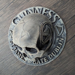 Może przedstawiać: Szara, dekoracyjna czaszka z logo Guinness i tekstem. Okrągły wz&oacute;r zawiera słowa "Guinness", "St. James's Gate Dublin" i "Traditionally Brewed". Czaszka ma pęknięcia i szczeg&oacute;łowe cechy.
