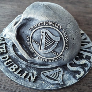 Może przedstawiać: Szary, teksturowany element dekoracyjny z napisem "TRADITIONALLY BREWED ST. JAMES'S GATE DUBLIN ESTO 1759" i symbolem harfy. Projekt ma wygląd postarzanego metalu.