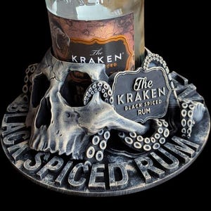 Könnte beinhalten: Ein dekorativer Flaschenhalter für eine Flasche Kraken Black Spiced Rum. Der Halter ist wie ein Schädel mit Tentakeln geformt und die Worte "The Kraken Black Spiced Rum" sind auf dem Halter zu sehen.