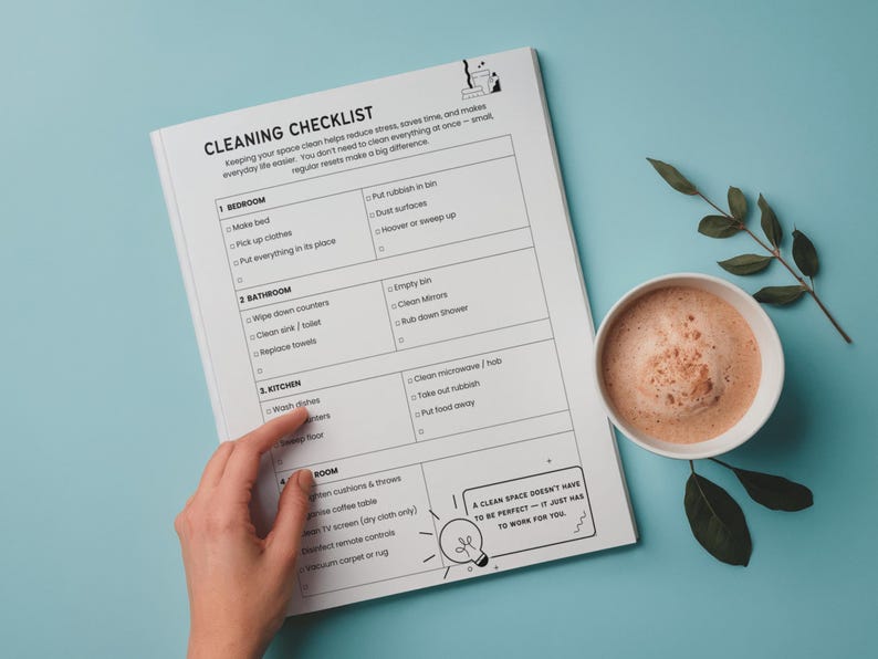 Pu&ograve; includere: Un elenco di controllo delle pulizie su carta bianca con sfondo blu. L'elenco include attivit&agrave; per la camera da letto, il bagno, la cucina e la stanza. Una tazza di caff&egrave; e un rametto di foglie sono a destra.