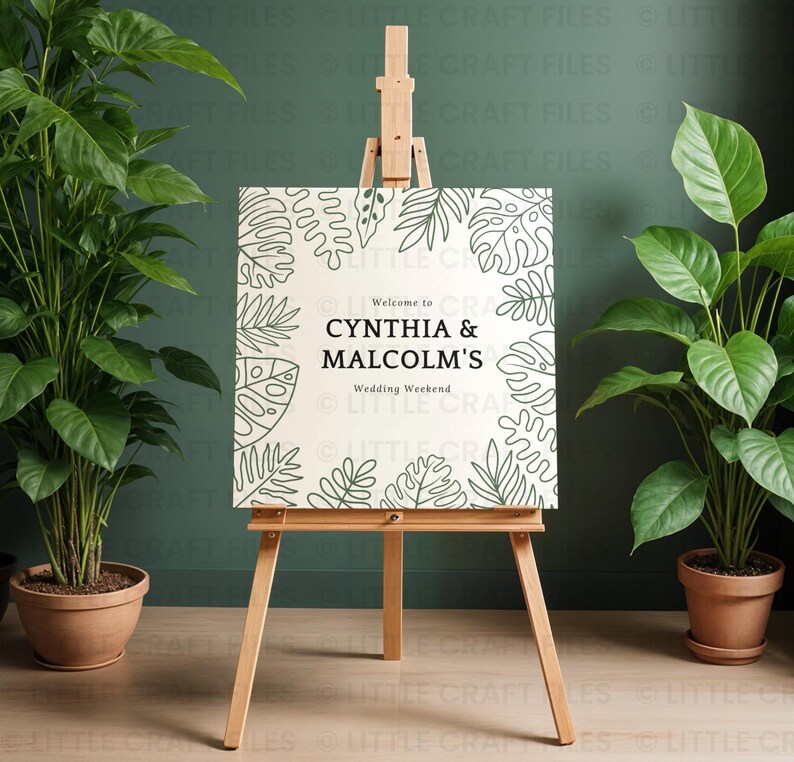 May include: A square white sign on a wooden easel featuring a black line art border of tropical leaves. The text reads Welcome to CYNTHIA & MALCOLM'S Wedding Weekend in black lettering. The sign is positioned between two potted green plants.
