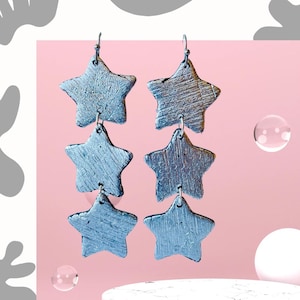 May include: Silver star-shaped dangle earrings with a textured finish. Each earring has three stars connected by a silver chain.