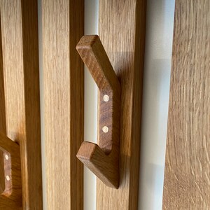 Könnte beinhalten: Nahaufnahme eines Holz-Kleiderständers mit mehreren Haken. Die Haken sind aus massivem Holz und haben eine natürliche Oberfläche. Der Ständer ist an einer weißen Wand montiert.
