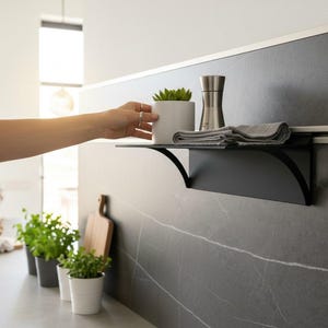 Könnte beinhalten: Ein Set aus drei Keramikbechern mit gesprenkelter, matter Oberfläche. Die Becher sind in Creme-, Hellgrau- und Dunkelgrautönen gehalten. Jeder Becher hat ein schlichtes, modernes Design und einen abgerundeten Henkel.