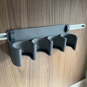 Peut inclure: Un porte-boîtes en plastique gris avec quatre fentes monté sur un mur. Le porte-boîtes est fixé à un rail métallique argenté.