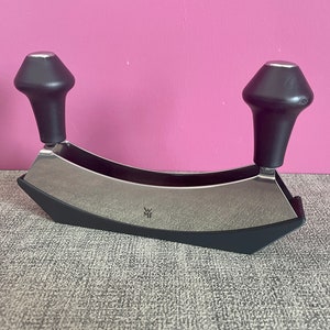 Könnte beinhalten: Ein silberner und schwarzer Fleischklopfer mit zwei schwarzen Griffen. Der Fleischklopfer hat die Buchstaben "WMF" auf der Vorderseite eingraviert.