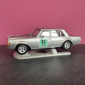 Könnte beinhalten: Ein silbernes Modellauto mit der grünen Nummer "11" an der Seite. Das Auto steht auf einem weißen Ständer.