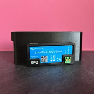 Może przedstawiać: Czarne urządzenie Victron Energy SmartShunt 500A/50mV z niebieskim wyświetlaczem, kodem QR i symbolem Bluetooth. Urządzenie ma zielony złącze i czarną obudowę.