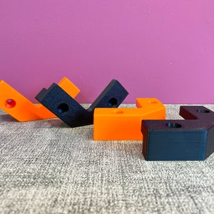 Könnte beinhalten: Vier 3D-gedruckte Eckwinkel, zwei sind schwarz und zwei sind orange. Die Winkel sind versetzt angeordnet.