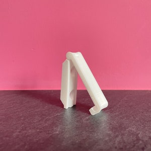 Può includere: Clip in plastica bianca con un design a cerniera. Il clip è aperto e pronto per l'uso.