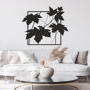 Peut inclure: Une décoration murale en métal noir représentant un cadre carré contenant une silhouette de feuilles d'érable et de branches. Le design est composé de lignes fines et de formes de feuilles pleines, créant un motif botanique sur le mur.