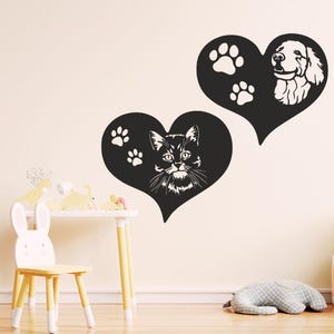 Peut inclure: Deux autocollants muraux noirs en forme de cœur présentant des silhouettes blanches d'animaux. Un cœur affiche une tête de chat avec deux empreintes de pattes, tandis que l'autre montre une tête de chien avec deux empreintes de pattes.