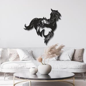 Peut inclure: Une décoration murale en métal noir représentant la silhouette de deux chevaux, un grand et un petit, positionnés ensemble avec des crinières et des queues fluides. Le motif est découpé dans une plaque de métal, créant un graphique sombre et détaillé.