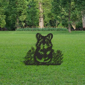 Peut inclure: Une silhouette en métal noir pour le jardin représentant un hamster tenant un petit objet, entouré de dessins au trait détaillés de diverses fleurs et feuillages, conçue pour être plantée dans une zone herbeuse.