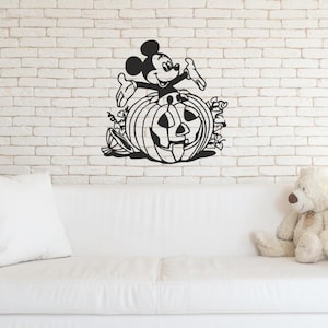 Peut inclure: Un autocollant mural noir représentant une illustration graphique de Mickey Mouse sortant d'une citrouille d'Halloween sculptée, entourée de feuilles et de vignes stylisées, appliqué sur un mur en briques blanches.