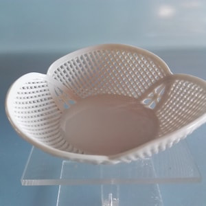 Puede incluir: Un cuenco de cerámica blanca con un delicado diseño calado. El cuenco tiene una forma redondeada y festoneada y es perfecto para servir pequeños aperitivos o postres.