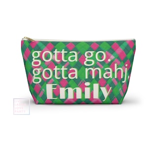 May include: A rectangular cosmetic bag with a green and pink plaid pattern. The bag features the text "gotta go. gotta mahj. Emily" in white. It has a gold zipper closure.