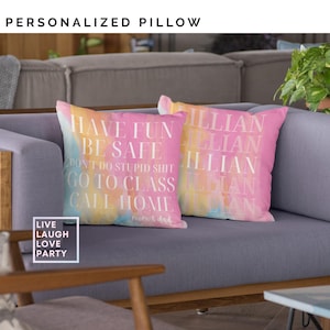 May include: Two pink and yellow tie-dye throw pillows with white text. The text on one pillow reads "Have Fun Be Safe Don't Do Stupid Shit Go To Class Call Home Mom & Dad". The text on the other pillow reads "illian" repeated five times.