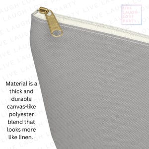 May include: Close-up of a gray canvas-like polyester blend pouch with a gold zipper. The material is thick and durable, resembling linen. The text on the pouch reads "Live Laugh Love Party".