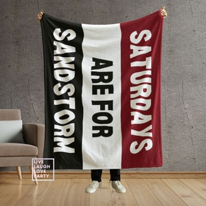 May include: A black, white, and red throw blanket with the text "Saturdays are for Sandstorm" printed on it.