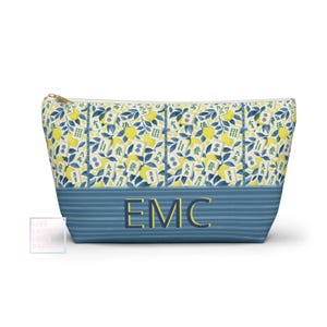 May include: A zippered cosmetic bag with a blue and yellow floral pattern. The bag features a blue striped bottom with the initials "EMC" in gold. The floral pattern includes lemons, leaves, and Chinese characters.