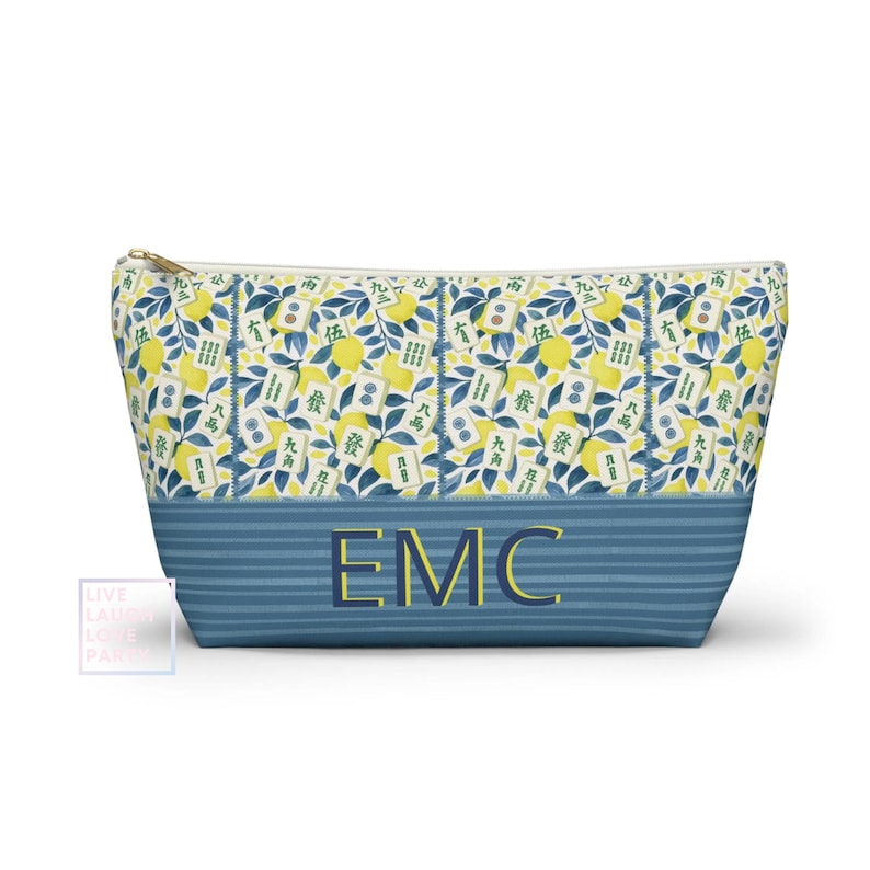 May include: A zippered cosmetic bag with a blue and yellow floral pattern. The bag features a blue striped bottom with the initials "EMC" in gold. The floral pattern includes lemons, leaves, and Chinese characters.