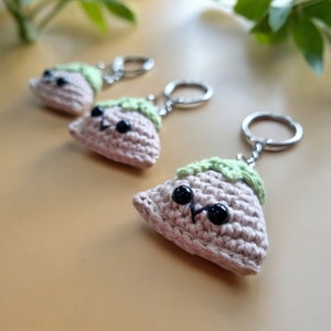 May include: Three crocheted keyrings shaped like a dumpling with a green leaf on top. Each keyring has a black button eye and a smiling mouth.