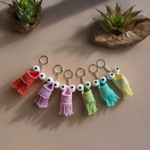 May include: Six crocheted keyrings with googly eyes and fringe. The keyrings are in various colours, including pink, green, blue, and yellow.