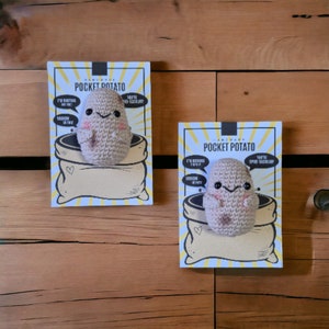 May include: Two handmade crocheted potato plushies on white cards with the text "Pocket Potato" and various phrases. The plushies are brown and have black eyes and a stitched smile.