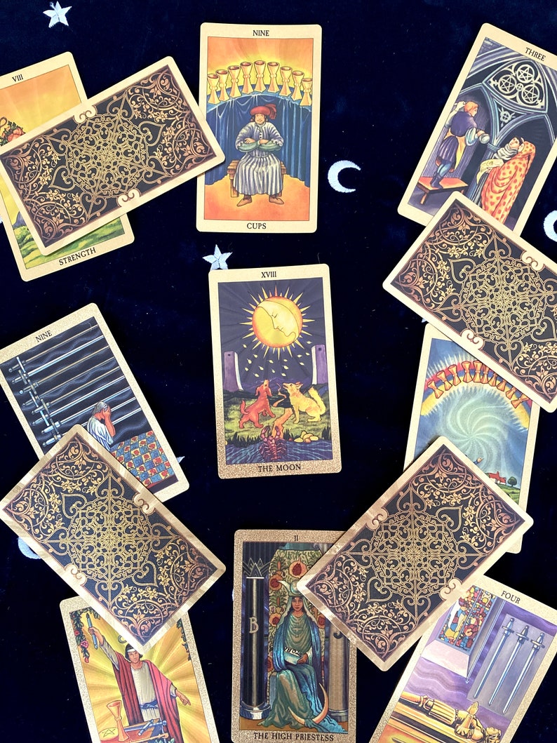 May include: Tarot card spread with ten cards, including The Moon, The High Priestess, Nine of Cups, Nine of Swords, Strength, Four of Swords, Three of Wands, and three cards with ornate gold designs.