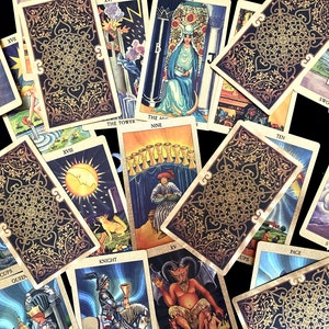 May include: A spread of tarot cards with gold and black designs. The cards include the Queen of Swords, the Nine of Cups, the Tower, the Knight of Cups, the Ten of Swords, the Page of Cups, the King of Cups, the Queen of Cups, the Devil, and the Moon.