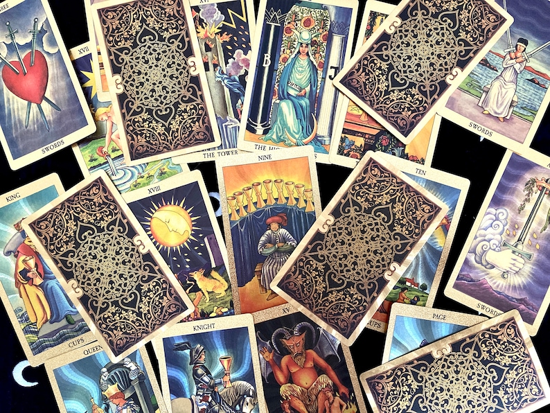May include: A spread of tarot cards with gold and black designs. The cards include the Queen of Swords, the Nine of Cups, the Tower, the Knight of Cups, the Ten of Swords, the Page of Cups, the King of Cups, the Queen of Cups, the Devil, and the Moon.