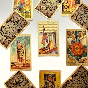 May include: A spread of ten tarot cards, including the Six of Swords, Wheel of Fortune, Page of Wands, and Seven of Wands. The cards are decorated with intricate gold and black designs.