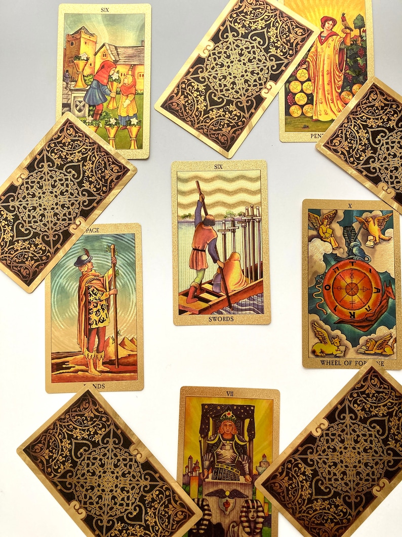 May include: A spread of ten tarot cards, including the Six of Swords, Wheel of Fortune, Page of Wands, and Seven of Wands. The cards are decorated with intricate gold and black designs.