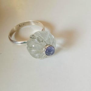 May include: A silver ring with a carved clear quartz stone and a small purple amethyst stone set in the center.