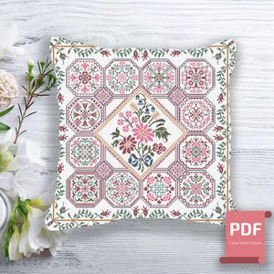 Peut inclure: Un coussin blanc avec un motif de point de croix représentant un motif floral dans des tons de rose, vert et marron. Le coussin est entouré d'un fond en bois blanc. Le texte "PDF Cross Stitch Pattern" est visible dans le coin inférieur droit.