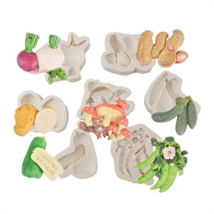 Könnte beinhalten: Eine Sammlung von Silikonformen mit verschiedenen Lebensmitteln. Die Formen umfassen Radieschen, Erdnüsse, Kartoffeln, Pilze, Zucchini und Erbsenschoten. Die Lebensmittel sind in leuchtenden Farben gehalten, die Formen in neutralem Grau.