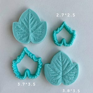 Può includere: Quattro formine per biscotti a forma di foglia turchese. Due sono stampi pieni e due sono contorni. Le dimensioni sono 2,7*2,5 cm, 3,7*3,5 cm e 3,8*3,5 cm. Le formine sono su una superficie bianca.
