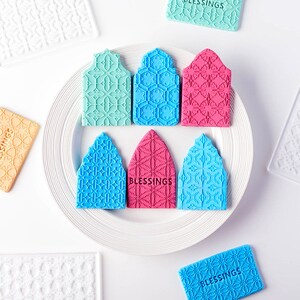 May include: A set of eight silicone stamps with intricate geometric patterns. The stamps are in various colors, including blue, green, pink, and white. The stamps are arranged on a white plate. One of the stamps has the word "Blessings" embossed on it.