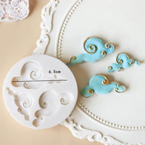 May include: White silicone mould with three cloud shapes, each with a swirl design. The mould measures 6.5 cm in diameter.