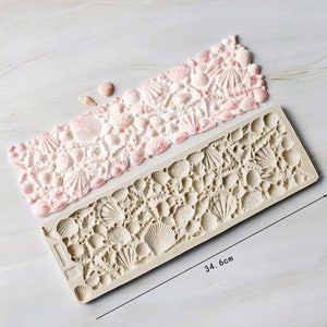May include: A silicone mould for baking seashell-shaped decorations. The mould is 34.6 cm long and features a variety of seashell designs.