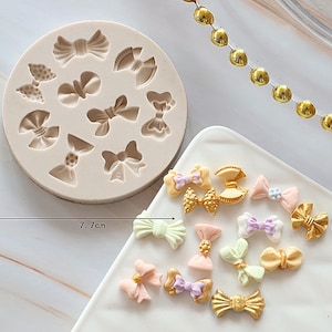 May include: A silicone mould with 12 different bow shapes for making fondant or gum paste decorations. The mould is 7 cm in diameter. There are also several finished bows in various colours, including pink, yellow, green, and gold.